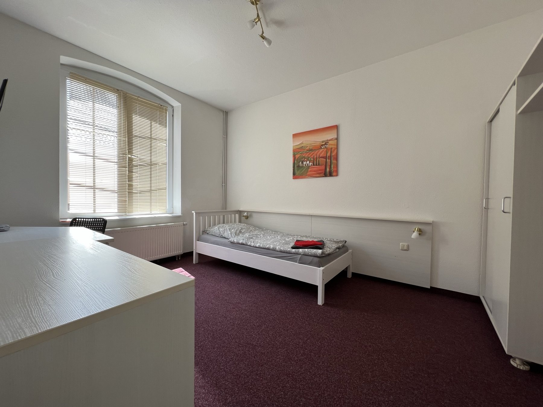 Einzelzimmer mit Schreibtisch, Bett und Fenster